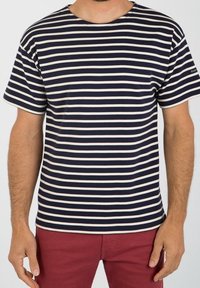 Navy and cream striped short-sleeve t-shirt with a round neck and soft fabric. Worn with red pants, featuring a small logo on the sleeve.