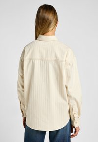 Camicia a maniche lunghe color crema con sottili strisce verticali, polsini con bottone e orlo arrotondato, realizzata in tessuto leggero.