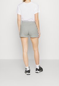 Shorts de algodón grises con cinturilla elástica, combinados con una camiseta blanca y zapatillas deportivas negras, vistos desde atrás.