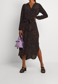 Dlouhé, tmavě hnědé šaty s leopardím potiskem, s páskem v oblasti pasu. S oficiálně s černými platformovými sandály a malou levandulovou kabelkou.
