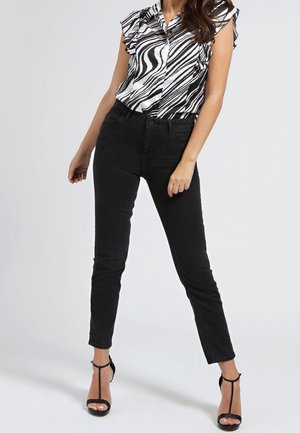 Jeans ajustados negros combinados con una blusa a rayas en blanco y negro que presenta mangas con volantes y un diseño de botones. Tacones negros de punta abierta.