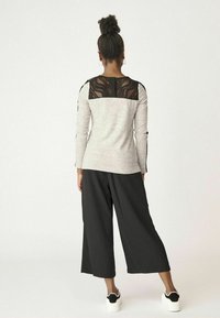 Šedý dlouhý rukáv s černým krajkovým zadním dílem, v kombinaci s černými kalhotami s širokým střihem a bílými teniskami, vytváří vrstvený a strukturovaný vzhled.