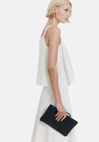 Clutch negro tejido sostenido en una mano, combinado con una blusa sin mangas de rayas blancas y una falda a juego, que presenta un corte holgado y una textura suave.