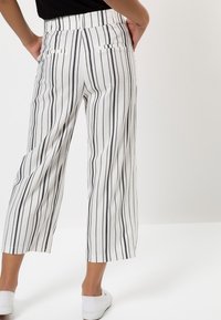 Pantalons crop blancs avec des rayures verticales noires, présentant une texture lisse, une taille ajustée et deux poches arrière. L'ourlet est droit.