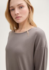 Losse grijze top van zacht materiaal, met een brede halslijn en verlaagde schouders. Gladde textuur met minimale stikseldetails.