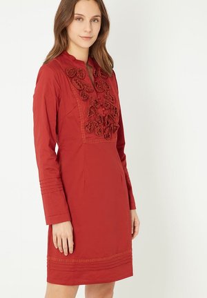 Vestido rojo con mangas largas, apliqué de tela floral en el pecho, detalles texturizados y corte recto. Presenta un cuello y líneas entalladas.