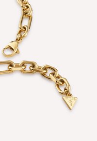 Bracciale in oro con grande collane, caratterizzato da una chiusura a moschettone e un’etichetta triangolare con la scritta "GUESS" in rilievo. Finitura liscia e lucida.
