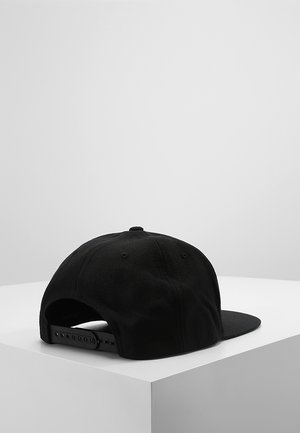 Czarna czapka typu snapback z regulowanym paskiem, umieszczona na białej kostce na jasnym, jednolitym tle.