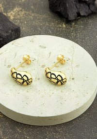 Goldene Ohrringe mit einem schwarzen geometrischen Muster, die eine glatte, abgerundete Form und einen klassischen Stecker auf einer strukturierten Oberfläche aufweisen.