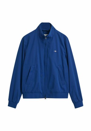 Blå zip-up jakke lavet af glat stof. Har en høj krave, elastiske manchetter, to forlommer og et lille logo på brystet.