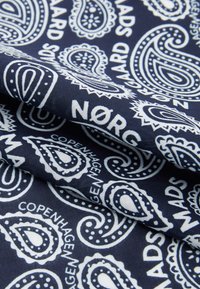 Tessuto blu navy con un motivo paisley bianco e testo. La texture è liscia, con dettagli di spirali e punti in un design ripetuto.