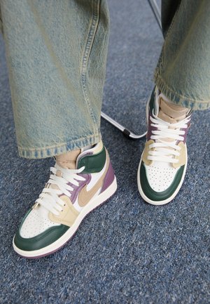 Hoch-top Sneaker mit grünen, schwarzen, beige und lila Lederakzenten, weißer perforierter Zehenpartie und cremefarbenen Schnürsenkeln. Getragen mit ausgebleichten blauen Jeans.