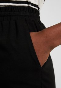 Joggers negros con cintura elástica y un bolsillo lateral con una mano visible. Tejido suave con una textura agradable.