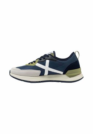 Zapatilla deportiva azul marino y oliva con logo X blanco lateral, cordones negros, suela beige y acento verde en el talón, vista lateral.