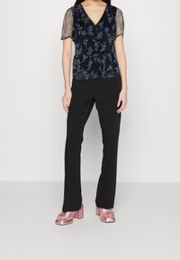 Blusa floreale blu marina con maniche corte trasparenti, abbinata a pantaloni neri aderenti e sandali con tacco a blocco rosa.