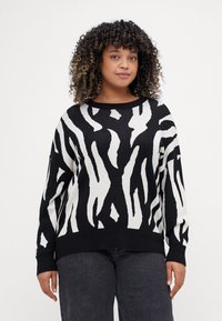 Μαύρη και λευκή ζαχαρωτή μπλούζα με σχέδιο ζέβρας, μακριά μανίκια, στρογγυλή λαιμόκοψη και λεπτομέρειες με ριμπ στο μανίκι και το τελείωμα. Μαλακό πλεκτό ύφασμα.