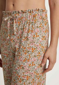 Bloemige pyjamabroek met een lichte achtergrond, versierd met roze, oranje en groene bloemen. Elastische tailleband met een gerimpelde rand.