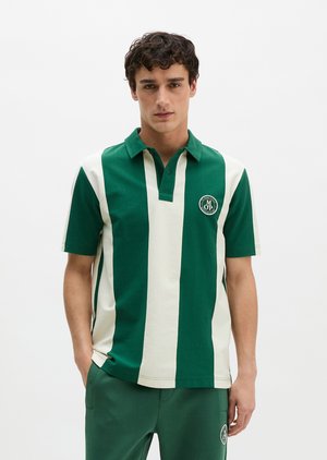 Mann trägt grünes und cremefarbenes Polohemd mit vertikalen Streifen und kleinem rundem Logo auf der Brust, kombiniert mit grünen Hosen.