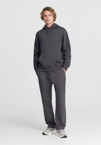 Felpa con cappuccio grigia e tasca frontale, abbinata a pantaloni jogger coordinati. Realizzata in tessuto morbido, con polsini e cintura elastici.