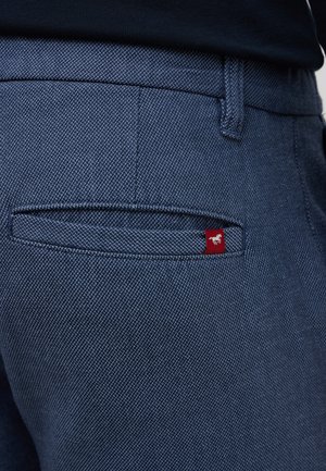 Granatowe dżinsy z fakturowanym splotem, pięcioma kieszeniami i małą czerwoną metką z białą grafiką na tylnej kieszeni.