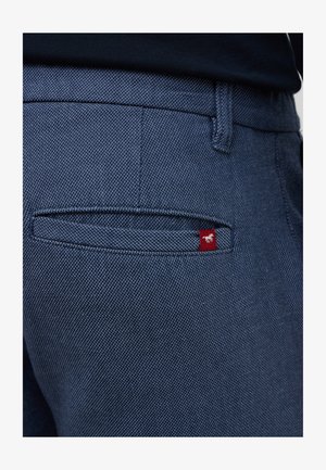 Granatowe dżinsy z fakturowanym splotem, pięcioma kieszeniami i małą czerwoną metką z białą grafiką na tylnej kieszeni.