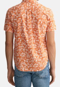 Camicia a maniche corte arancione a fiori con motivi bianchi, colletto con bottoni e orlo curvo. Realizzata in un tessuto traspirante con una vestibilità comoda.