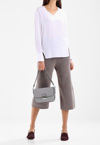 Bílý dlouhý rukáv top s véčkovým výstřihem, šedé strakaté široké kalhoty, šedá kabelka se stříbrným kováním a burgundské nazouvací boty s výřezy.