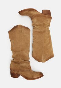 Bottes hautes en suède beige au design décontracté, à bout pointu et talon en bois. Coutures notables le long de la tige et de la couture arrière.