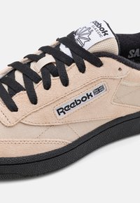 Baskets en daim beige avec lacets noirs, embout texturé et semelle en caoutchouc noire. Présentent le logo Reebok sur le côté et un marquage classique sur la languette.