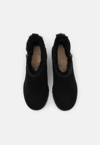 Bottines en daim noir avec doublure en fourrure douce, détail zippé sur le côté, bout arrondi et semelle texturée. Design épuré et simple, sans motifs visibles.