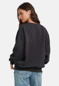 Czarny, oversize sweter z okrągłym dekoltem i luźnym krojem. Rybrowane mankiety i dół. Połączony z jasnoniebieskimi dżinsami. Miękka faktura.