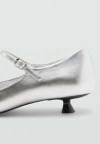 Scarpa Mary Jane in pelle argentata con tacco a cono nero piccolo e una sottile cinghia alla caviglia con fibbia. Finitura liscia e metallica.