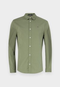 Maglietta verde a maniche lunghe in un morbido tessuto di cotone. Presenta un colletto classico, chiusura con bottone e un piccolo logo sulla parte petto.
