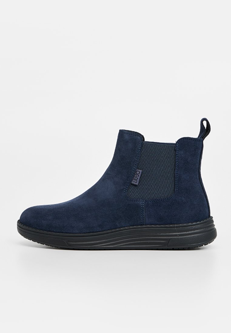 Bottines en daim bleu marine avec des panneaux élastiques sur les côtés, bout rond, languette de traction et une semelle noire en caoutchouc texturé.