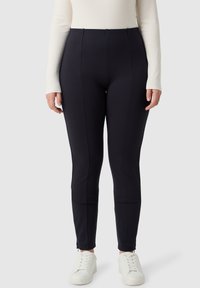 Czarne legginsy z wysokim stanem, wykonane z elastycznego materiału, z prostymi liniami, szwami bocznymi i zamkami błyskawicznymi przy kostkach, zestawione z białymi sneakerkami.