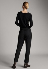 Schwarzer gestrickter Pullover mit rundem Ausschnitt, kombiniert mit locker sitzenden schwarzen Hosen mit elastischem Bund und umgeschlagenen Bündchen. Braune Stiefeletten.