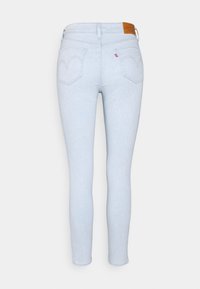 Jeans ajustados de color azul claro con cinco bolsillos, que presentan una etiqueta de cuero en la cintura y un patrón de costura distintivo en el bolsillo trasero.