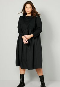 Černé šaty s dlouhým rukávem, kulatým výstřihem a detailem s nabíraným pasem. Vyrobené z hladké, lehké tkaniny, s uvolněným, splývavým střihem.
