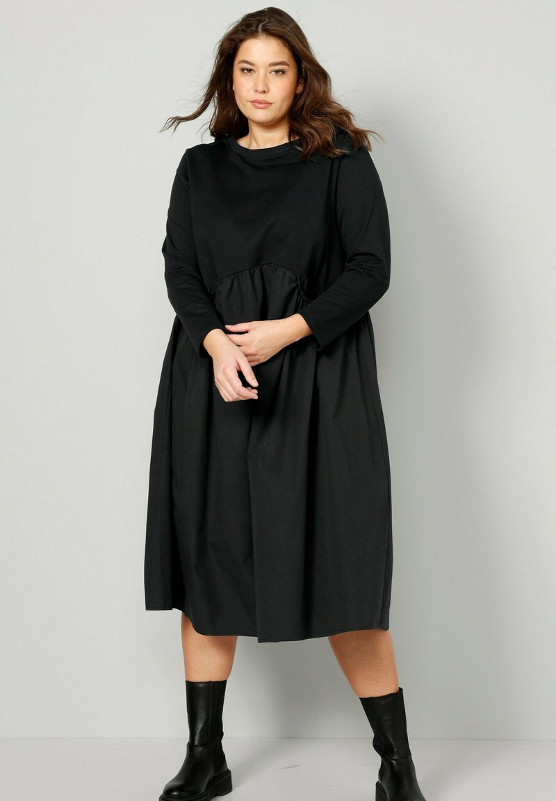 Černé šaty s dlouhým rukávem, kulatým výstřihem a detailem s nabíraným pasem. Vyrobené z hladké, lehké tkaniny, s uvolněným, splývavým střihem.