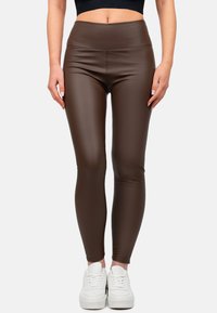 Leggings marroni a vita alta realizzati in un materiale lucido, con un design aderente e una texture liscia, abbinati a sneaker bianche.