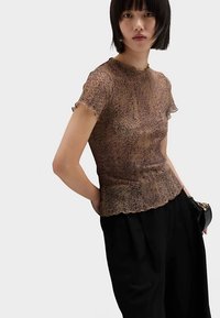 Brun leopardmönstrad topp med korta ärmar, vågiga kanter, smal passform, något genomskinlig med ett strukturerat tyg. Kombinerad med svarta vida byxor.