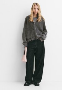 Grå ribbet cardigan med frontlommer, parret med løse sorte jeans. En lys rosa håndtaske fremhæver det afslappede look. Blød stofstruktur.