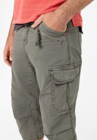 Cargo-Shorts aus olivgrünen Stoff mit mehreren Taschen, sichtbarem Nahtdetail und einer Reißverschlusstasche an der Seite.