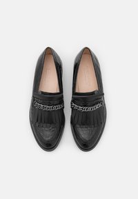 Mocassins en cuir noir à motif crocodile avec des franges et un détail en chaîne argentée, semelles intérieures beiges douces, disposés côte à côte sur un fond blanc.