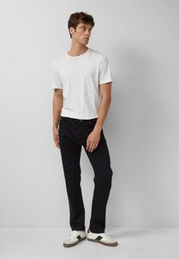 Dunkelblaue Jeans im Slim Fit, kombiniert mit einem schlichten weißen T-Shirt und lässigen weißen Sneakern. Glatter Stoff mit minimaler Detailgestaltung.