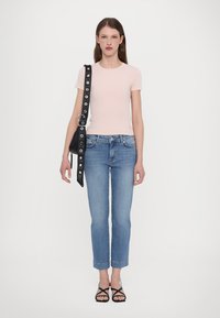T-shirt ajustada de malha em rosa claro, combinada com jeans de lavagem média, sandálias strappy pretas e uma bolsa preta com detalhes em hardware circular.