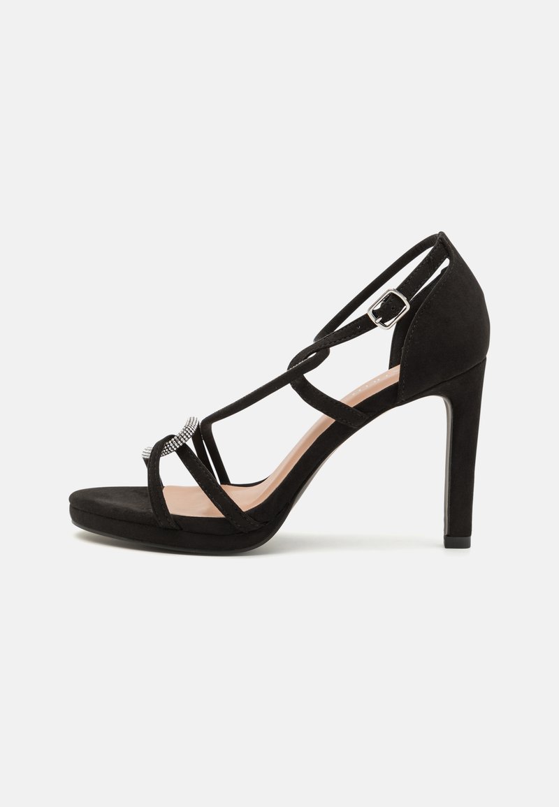 Black suede high-heeled sandal with crisscross straps, a decorative silver-tone accent, and a platform sole for added height.