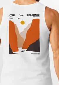 White tank top featuring a graphic design of a canyon with orange and brown cliffs, a yellow sun, and a kayaker on a river below.