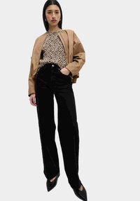 Giacca bomber marrone su una maglia beige con stampa leopardata, pantaloni neri a vita alta e scarpe nere con punta appuntita. Texture lisce, vestibilità moderna.
