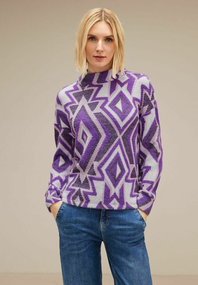 Maglione a motivo viola e grigio con collo alto e maniche lunghe, caratterizzato da forme geometriche e una texture morbida. Abbinato a jeans blu.